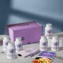 A product bundle display for GleeFull Supplements on a marble surface against a blue background. The layout includes a large purple shipping box featuring the slogan 'FEEL LIKE YOURSELF AGAIN.', three white bottles of Over 30 Hormone Support and three white bottles of Meno Belly Flusher, a purple branded pen, a matching notepad that reads 'REMINDERS WHEN I'M HAVING A MENOPAUSE MOMENT', and a recipe booklet titled 'THE MENOPAUSE Recipes'