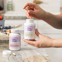 A hand holding a golden supplement capsule against a light gray background. Pink and purple headline text reads '#1 All-Natural Hormone Balancing Supplement.' A purple circular badge reads 'How to Use: Take 2 capsules in the morning or night for lasting balance.'
